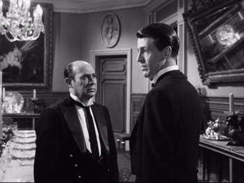 Movie still from “The Exterminating Angel” (1962), directed by Luis Buñuel – Two men in suits are talking in a room; Medium shot, Over the shoulder angle