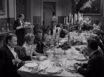 Movie still from “The Exterminating Angel” (1962), directed by Luis Buñuel – A black and white photo of people sitting at a dinner table; Wide shot, High angle