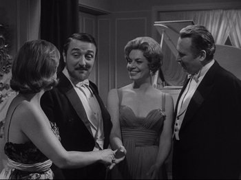 Movie still from “The Exterminating Angel” (1962), directed by Luis Buñuel – A group of people standing next to each other in front of a piano; Medium shot, Over the shoulder angle