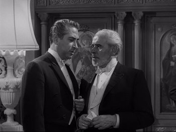 Movie still from “The Exterminating Angel” (1962), directed by Luis Buñuel – A man and a man in a suit talking to each other; Medium shot, Low angle