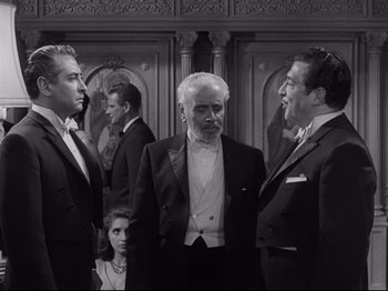 Movie still from “The Exterminating Angel” (1962), directed by Luis Buñuel – A black and white photo of a group of men in tuxedos; Medium shot, Over the shoulder angle