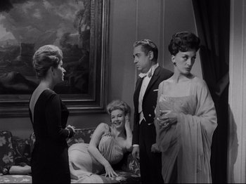 Movie still from “The Exterminating Angel” (1962), directed by Luis Buñuel – A group of people standing in a living room next to each other; Medium shot, Over the shoulder angle