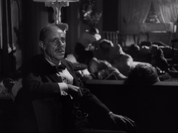 Movie still from “The Exterminating Angel” (1962), directed by Luis Buñuel – An older man sitting in a chair in front of a window; Medium shot, Low angle