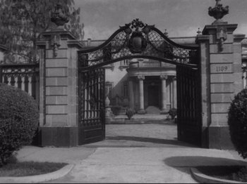 Movie still from “The Exterminating Angel” (1962), directed by Luis Buñuel – An open gate leading to an old building; Extreme Wide shot, Low angle