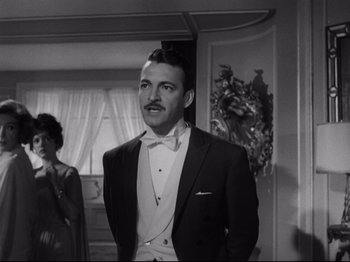 Movie still from “The Exterminating Angel” (1962), directed by Luis Buñuel – A man in a tuxedo standing next to a woman in a suit; Medium shot, Low angle