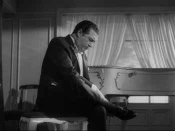 Movie still from “The Exterminating Angel” (1962), directed by Luis Buñuel – A black and white photo of a man sitting on a chair; Medium shot, Low angle