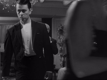 Movie still from “The Exterminating Angel” (1962), directed by Luis Buñuel – A black and white photo of a man in a tuxedo; Medium shot, Over the shoulder angle