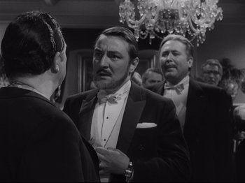 Movie still from “The Exterminating Angel” (1962), directed by Luis Buñuel – A black and white photo of a man in a tuxedo; Medium shot, Over the shoulder angle