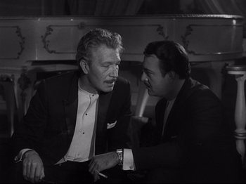 Movie still from “The Exterminating Angel” (1962), directed by Luis Buñuel – Two men in suits talking to each other in front of a fireplace; Medium shot, High angle