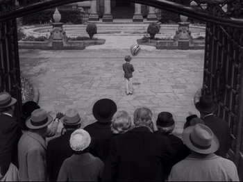 Movie still from “The Exterminating Angel” (1962), directed by Luis Buñuel – A group of people standing in a courtyard watching a boy throw a frisbee; Wide shot, High angle