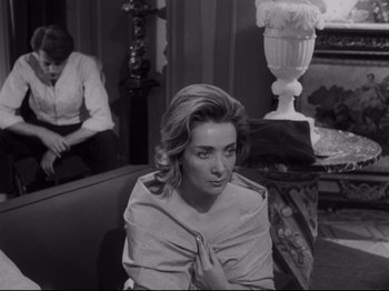 Movie still from “The Exterminating Angel” (1962), directed by Luis Buñuel – A black and white photo of a woman sitting on a couch; Medium shot, Over the shoulder angle