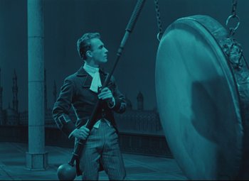 Movie still from “The Fabulous Baron Munchausen” (1962), directed by Karel Zeman – A man in a suit and tie standing next to a large metal object; Medium shot, Low angle