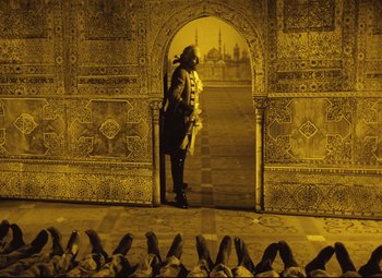 Movie still from “The Fabulous Baron Munchausen” (1962), directed by Karel Zeman – A man standing in front of an archway with pigeons; Wide shot, Low angle