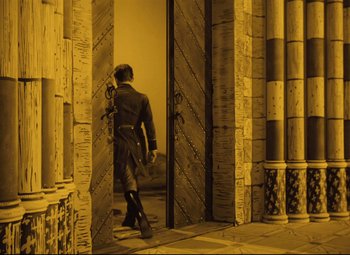 Movie still from “The Fabulous Baron Munchausen” (1962), directed by Karel Zeman – A man standing in front of a door way; Wide shot, High angle