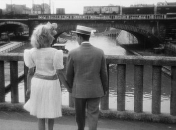 Movie still from “The Fiancés of the Bridge Mac Donald” (1961), directed by Agnès Varda – A man and a woman standing next to each other on a bridge; Wide shot, High angle