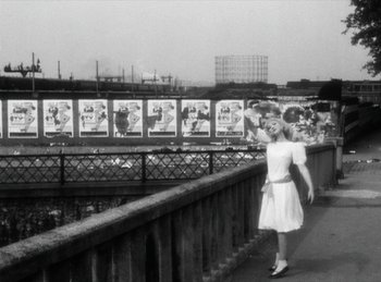 Movie still from “The Fiancés of the Bridge Mac Donald” (1961), directed by Agnès Varda – A black and white photo of a woman walking on a bridge; Wide shot, Low angle