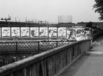 Movie still from “The Fiancés of the Bridge Mac Donald” (1961), directed by Agnès Varda – A black and white photo of a bridge with a lot of posters on it; Extreme Wide shot, Low angle