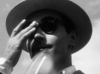 Movie still from “The Fiancés of the Bridge Mac Donald” (1961), directed by Agnès Varda – A man wearing a sun hat and holding a wine glass; Close Up shot, Low angle