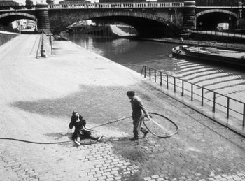 Movie still from “The Fiancés of the Bridge Mac Donald” (1961), directed by Agnès Varda – A man and a woman washing a boat in a river; Extreme Wide shot, High angle