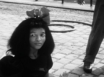 Movie still from “The Fiancés of the Bridge Mac Donald” (1961), directed by Agnès Varda – A young girl with a bow on her head sitting on the sidewalk; Close Up shot, High angle