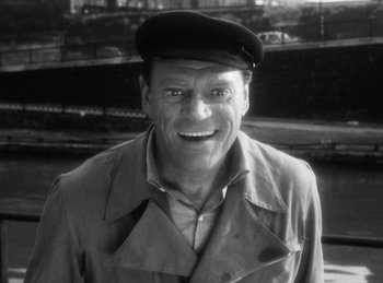 Movie still from “The Fiancés of the Bridge Mac Donald” (1961), directed by Agnès Varda – An older man wearing a hat smiling for the camera; Close Up shot, High angle