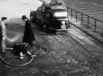 Movie still from “The Fiancés of the Bridge Mac Donald” (1961), directed by Agnès Varda – An old photo of a woman on the street with a bicycle; Wide shot, High angle