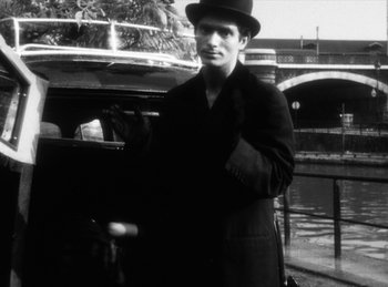 Movie still from “The Fiancés of the Bridge Mac Donald” (1961), directed by Agnès Varda – A black and white photo of a man wearing a hat; Medium shot, Low angle
