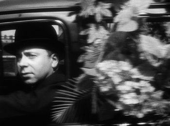 Movie still from “The Fiancés of the Bridge Mac Donald” (1961), directed by Agnès Varda – A black and white photo of a man in the back of a car; Close Up shot, Over the shoulder angle