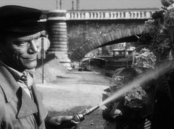 Movie still from “The Fiancés of the Bridge Mac Donald” (1961), directed by Agnès Varda – An old photo of a man spraying water from a hose; Close Up shot, Over the shoulder angle