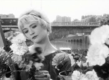Movie still from “The Fiancés of the Bridge Mac Donald” (1961), directed by Agnès Varda – A black - and - white photo of a woman holding flowers; Close Up shot, Over the shoulder angle