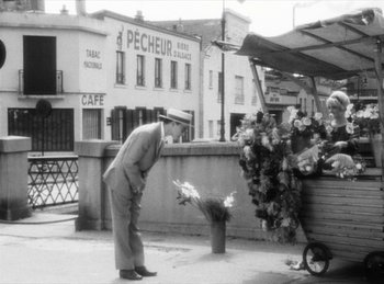 Movie still from “The Fiancés of the Bridge Mac Donald” (1961), directed by Agnès Varda – An old black and white photo of a man looking at flowers; Wide shot, High angle