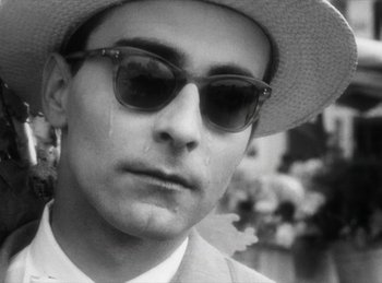 Movie still from “The Fiancés of the Bridge Mac Donald” (1961), directed by Agnès Varda – A black and white photo of a man wearing a hat and sunglasses; Close Up shot, Low angle