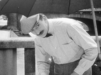 Movie still from “The Fiancés of the Bridge Mac Donald” (1961), directed by Agnès Varda – An old photo of a man holding an umbrella; Medium shot, High angle