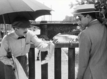 Movie still from “The Fiancés of the Bridge Mac Donald” (1961), directed by Agnès Varda – Two men are standing on a bridge and one is holding an umbrella; Medium shot, Over the shoulder angle