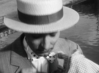 Movie still from “The Fiancés of the Bridge Mac Donald” (1961), directed by Agnès Varda – A black and white photo of a man wearing a hat and bow tie; Close Up shot, High angle