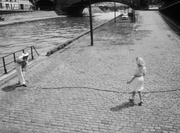 Movie still from “The Fiancés of the Bridge Mac Donald” (1961), directed by Agnès Varda – Two people are playing tennis on a cobble stone street; Extreme Wide shot, High angle