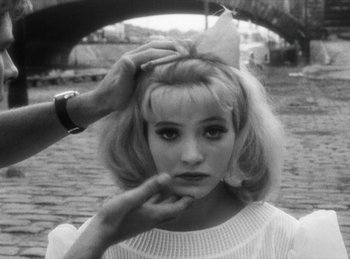 Movie still from “The Fiancés of the Bridge Mac Donald” (1961), directed by Agnès Varda – A black - and - white photo of a woman with a bow in her hair; Close Up shot, Over the shoulder angle