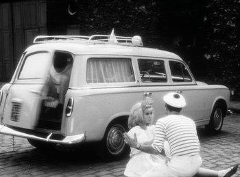 Movie still from “The Fiancés of the Bridge Mac Donald” (1961), directed by Agnès Varda – An old photo of a man and a woman sitting in front of an old van; Wide shot, High angle