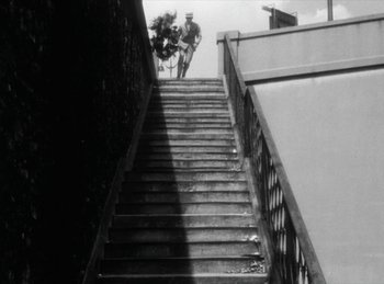 Movie still from “The Fiancés of the Bridge Mac Donald” (1961), directed by Agnès Varda – A man riding a bike down the side of a set of stairs; Extreme Wide shot, Low angle