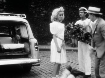 Movie still from “The Fiancés of the Bridge Mac Donald” (1961), directed by Agnès Varda – A man and a woman standing next to each other on a brick road; Wide shot, Over the shoulder angle