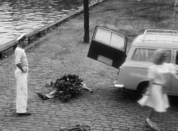 Movie still from “The Fiancés of the Bridge Mac Donald” (1961), directed by Agnès Varda – An old photo of a woman walking on a brick road with a car; Wide shot, High angle