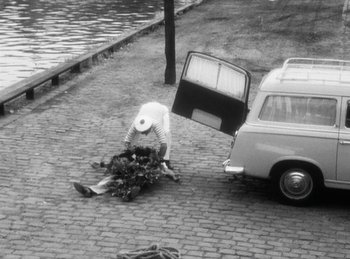 Movie still from “The Fiancés of the Bridge Mac Donald” (1961), directed by Agnès Varda – An old photo of a man picking up flowers from the ground; Wide shot, High angle