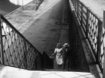 Movie still from “The Fiancés of the Bridge Mac Donald” (1961), directed by Agnès Varda – A man and a woman walking up a flight of stairs; Wide shot, High angle