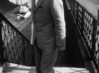 Movie still from “The Fiancés of the Bridge Mac Donald” (1961), directed by Agnès Varda – A black and white photo of a man in a suit walking down the stairs; Medium shot, High angle