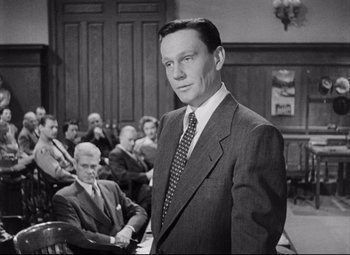 Movie still from “The File on Thelma Jordon” (1949), directed by Robert Siodmak – A man standing in front of a group of people; Medium shot, Over the shoulder angle