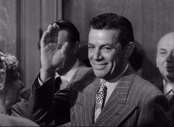 Movie still from “The File on Thelma Jordon” (1949), directed by Robert Siodmak – A black and white photo of a man in a suit waving; Medium shot, Over the shoulder angle