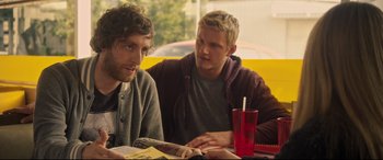 Movie still from “The Final Girls” (2015), directed by Todd Strauss-Schulson – Two young men sitting at a table with a magazine; Medium shot, Over the shoulder angle