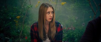 Movie still from “The Final Girls” (2015), directed by Todd Strauss-Schulson – A young woman in a plaid shirt sitting in front of flowers; Close Up shot, High angle