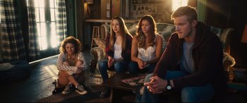 Movie still from “The Final Girls” (2015), directed by Todd Strauss-Schulson – A group of people sitting around a living room together; Medium shot, Over the shoulder angle
