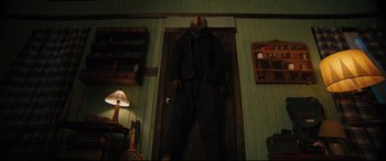 Movie still from “The Final Girls” (2015), directed by Todd Strauss-Schulson – A man in a black jacket is standing in front of a door; Wide shot, Low angle